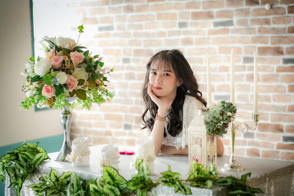 A woman elegantly posing at a table adorned with flowers and candles.