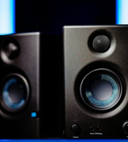 Close-up of modern black loudspeakers with blue accents in a studio setting.